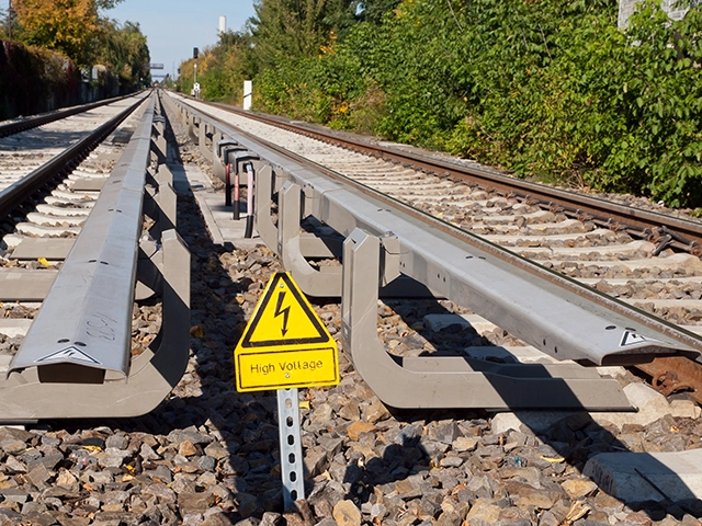 Railroad tracks with special attention to the conductor rail and the "High voltage, danger to life" sign.